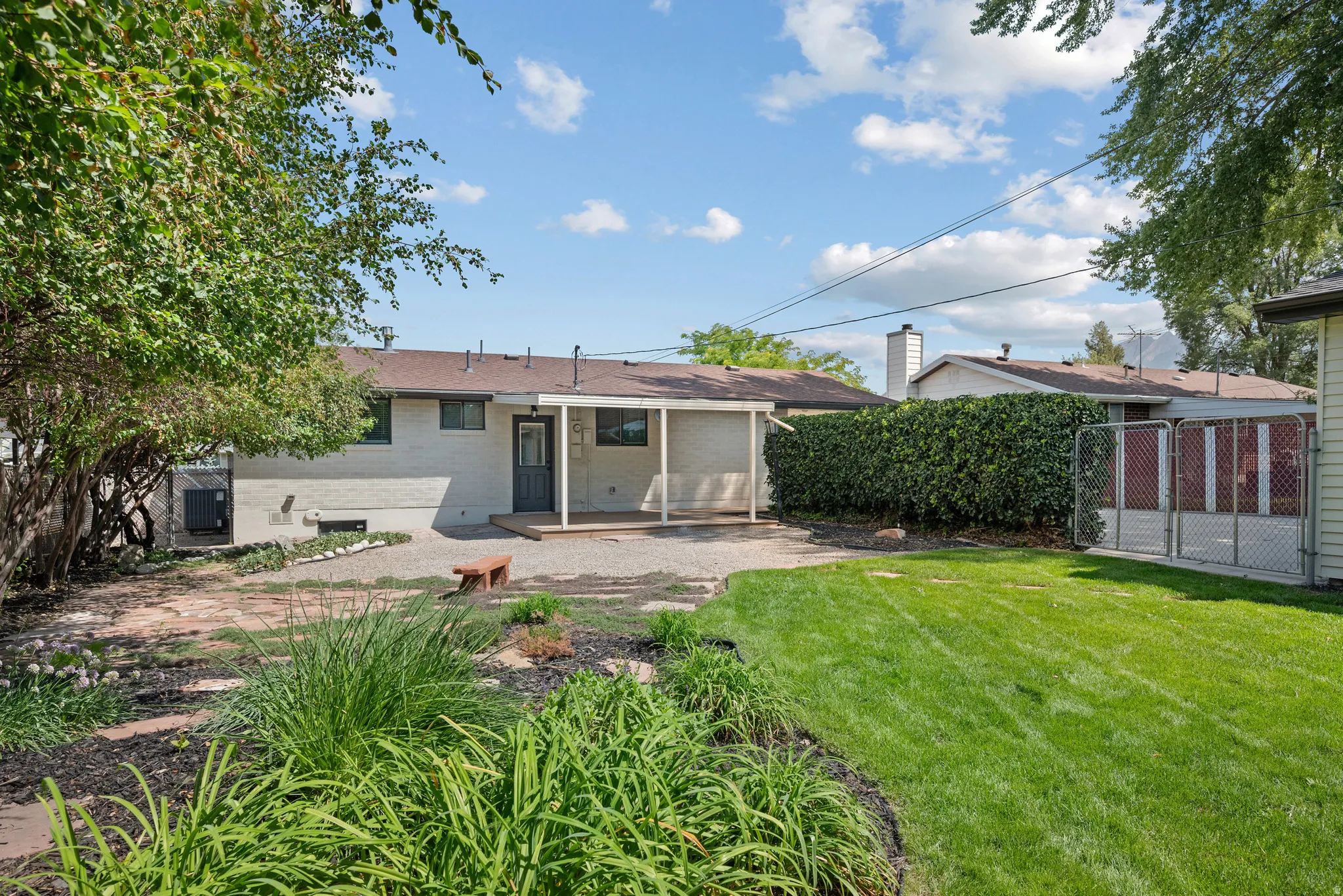 Expansive backyard featuring a covered patio, landscaped garden beds, and manicured lawn