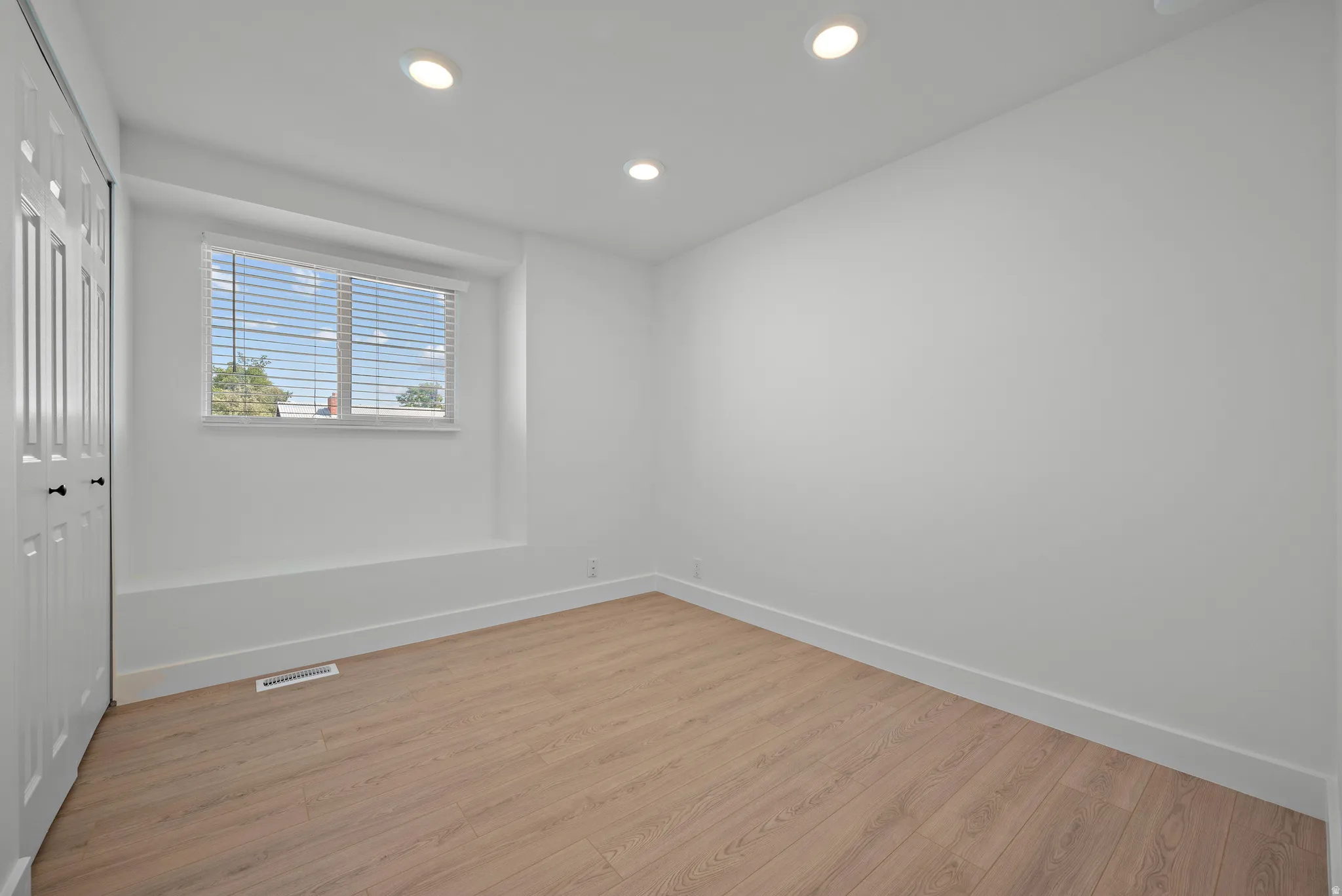 Recessed ceiling lighting, wood-finish flooring, white walls, and a window with blinds