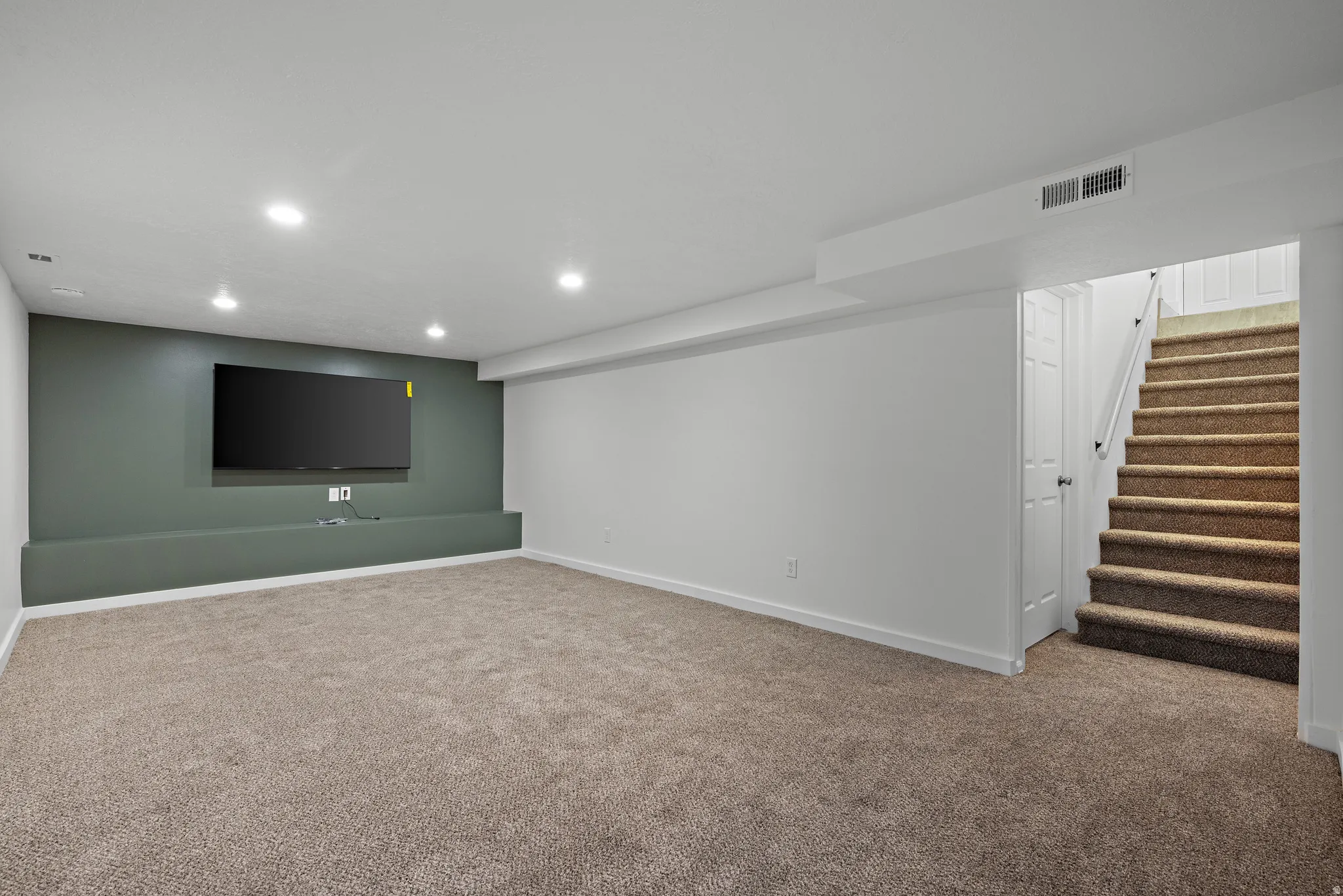 Recessed lighting, carpeted flooring, built-in media shelf, white trim, and a staircase with carpeted treads