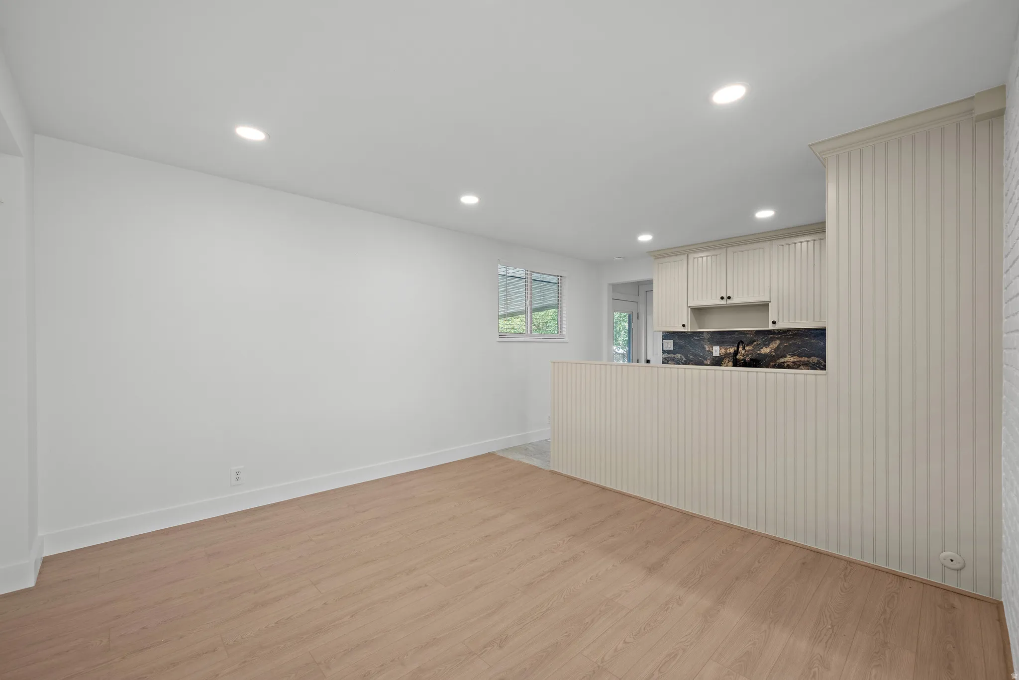 Open concept living area with wood-finish flooring, recessed lighting, and a kitchen featuring white cabinetry, a dark backsplash, and a breakfast bar