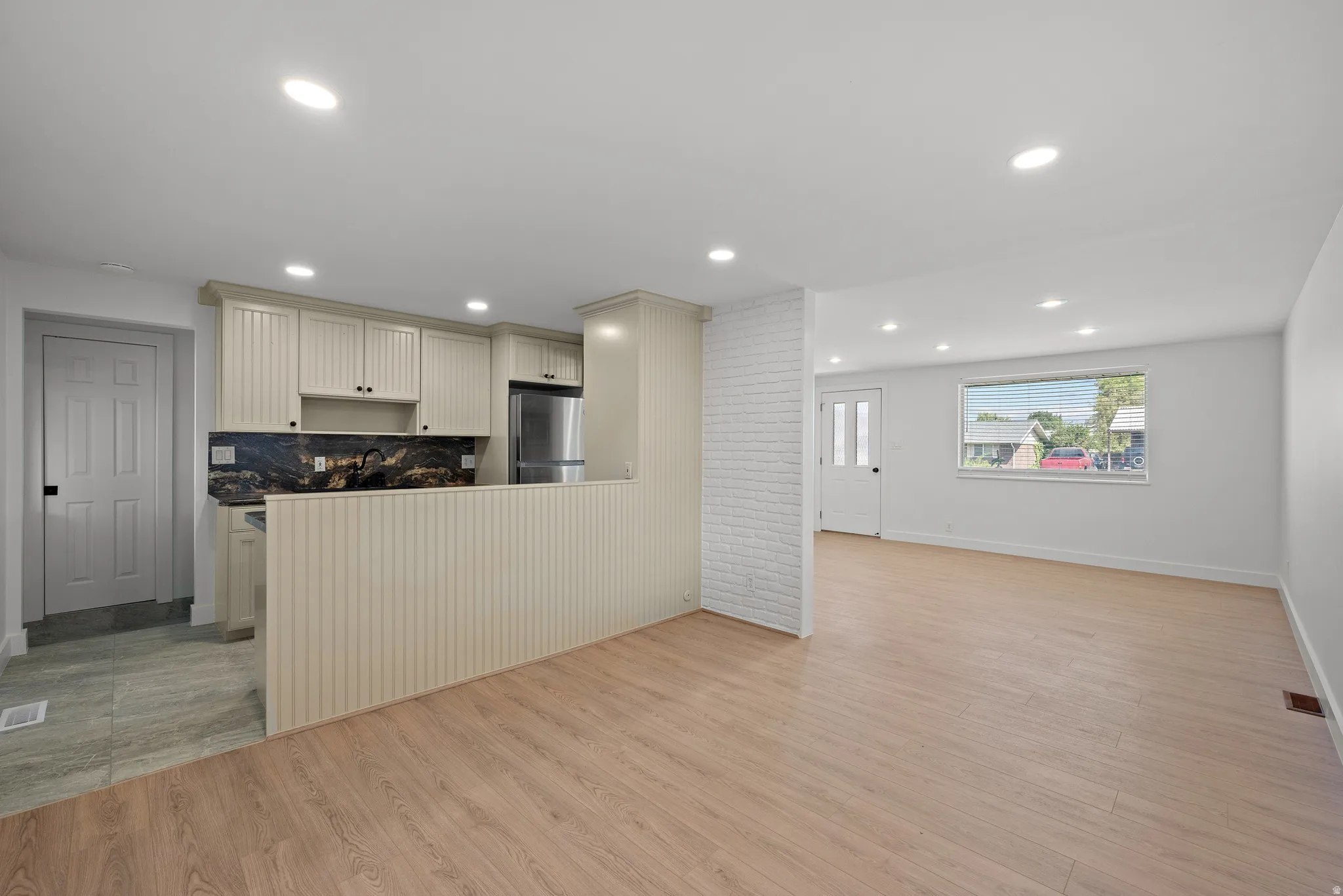 Kitchen with light-colored cabinetry, stainless steel refrigerator, and dark stone backsplash