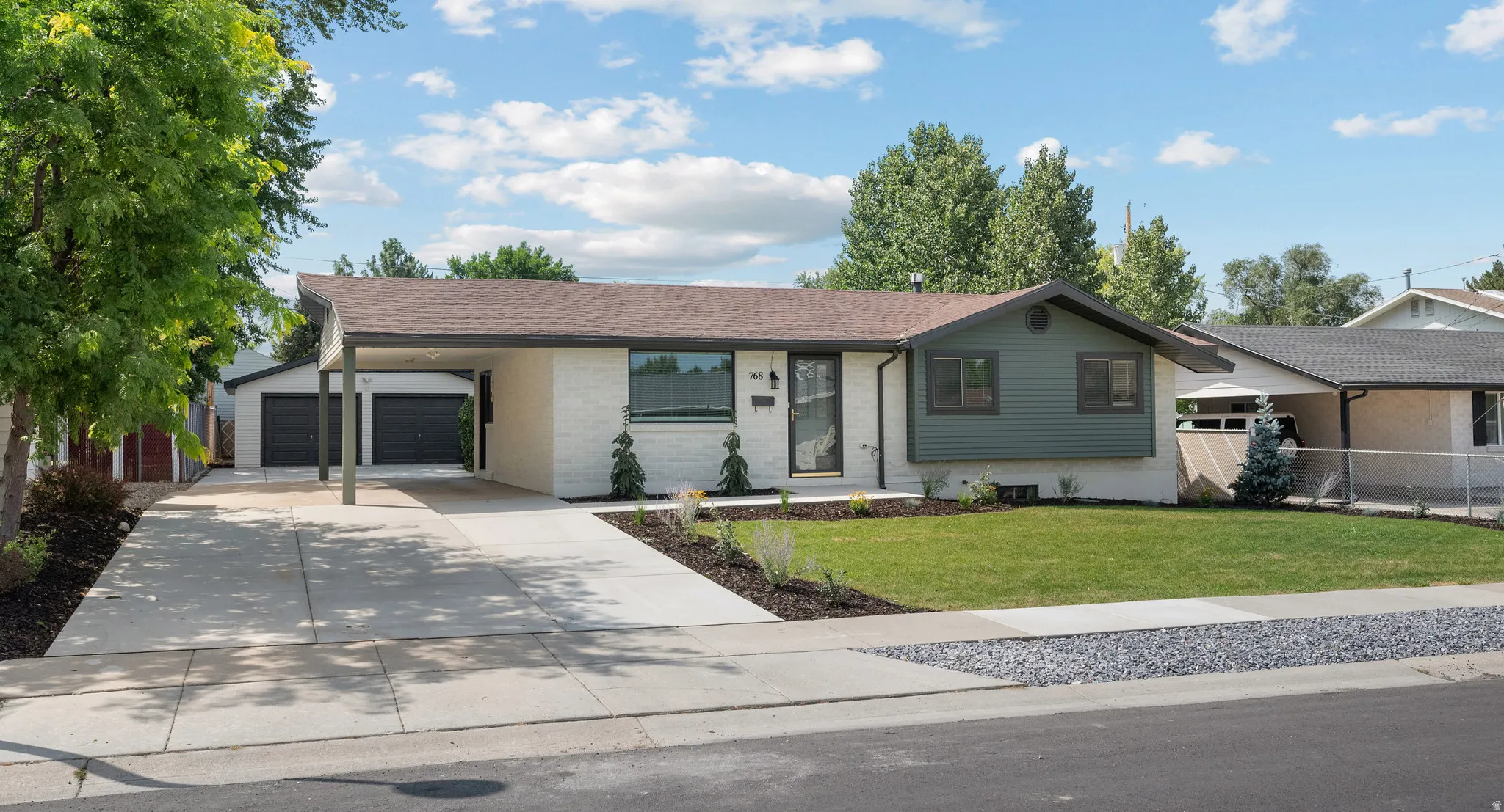 Light-colored brick exterior with dark trim accents, a front lawn, and a wide concrete driveway