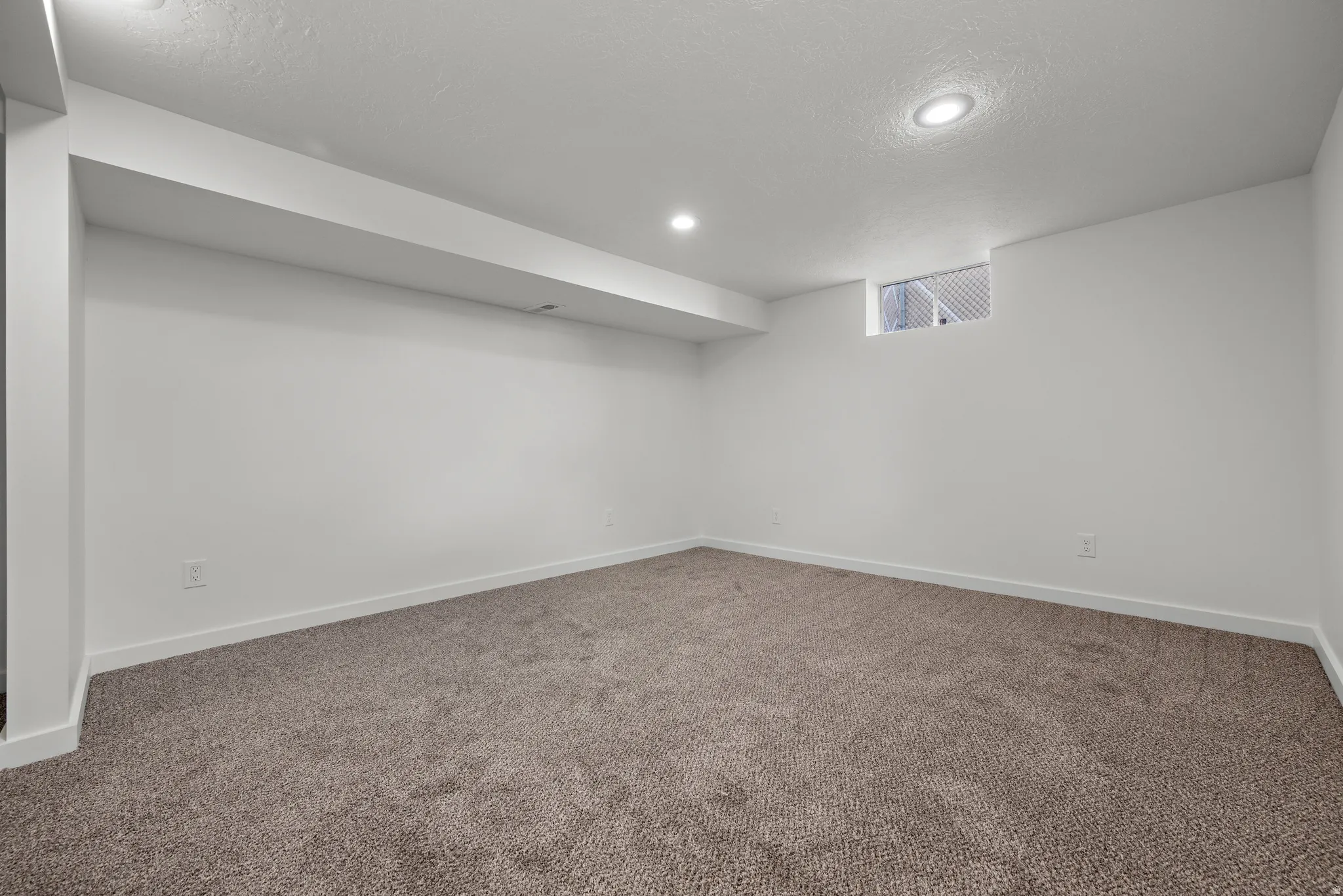 Recessed lighting illuminates a carpeted room with white walls and a window