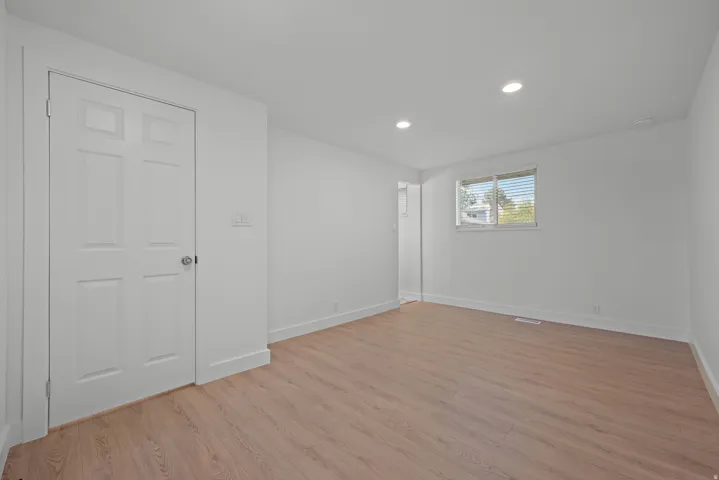Spacious room featuring wood-finish flooring, recessed lighting, and a multi-pane window with blinds