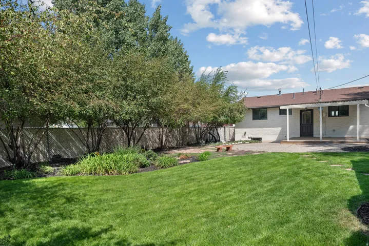 Expansive backyard featuring a manicured lawn, established trees, and a chain-link fence