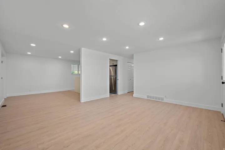 Recessed ceiling lighting, light wood-finish flooring, white painted walls, and a stainless steel refrigerator