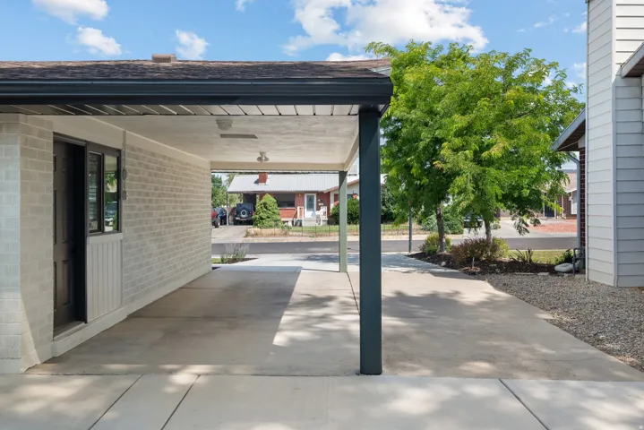 Covered carport with concrete flooring, light brick exterior, and a dark brown door