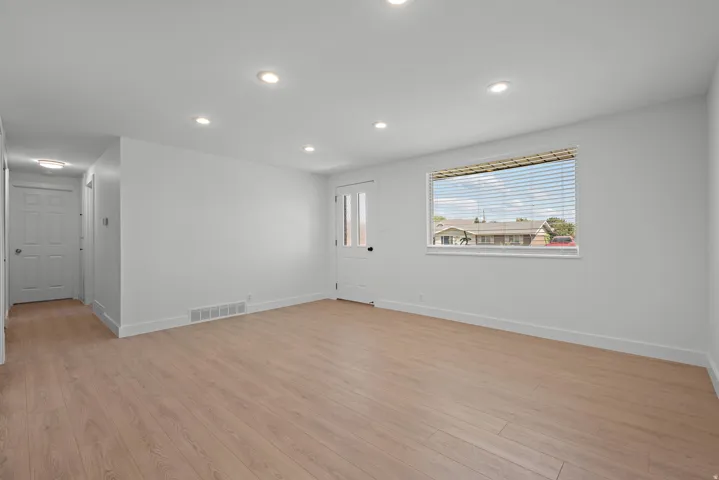 Light wood-finish flooring with white baseboards, recessed ceiling lighting, and a window with blinds