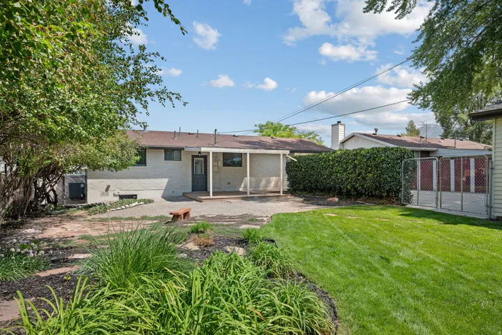 Expansive backyard featuring a covered patio, landscaped garden beds, and manicured lawn