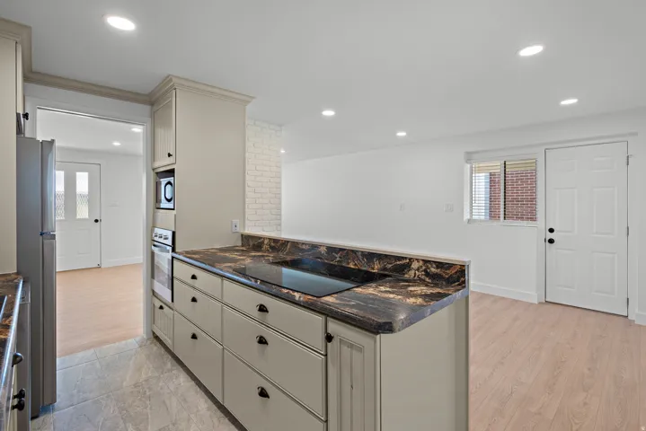 Kitchen featuring light-toned cabinetry with dark hardware, dark stone countertops, an integrated cooktop, and built-in microwave