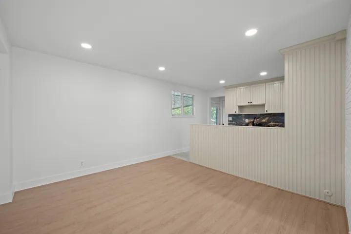 Open concept living area with wood-finish flooring, recessed lighting, and a kitchen featuring white cabinetry, a dark backsplash, and a breakfast bar