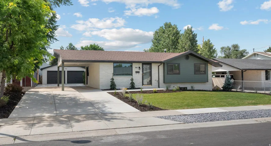 Light-colored brick exterior with dark trim accents, a front lawn, and a wide concrete driveway