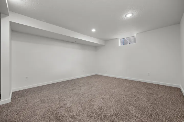 Recessed lighting illuminates a carpeted room with white walls and a window