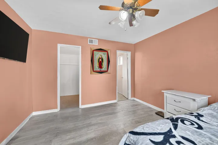 Wood-finish flooring with white trim, ceiling fan with integrated lighting, and a wall-mounted display