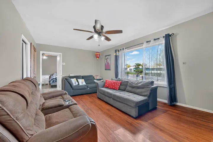 Wood-finish flooring throughout, ceiling fan with integrated lighting, and a large window providing ample natural light