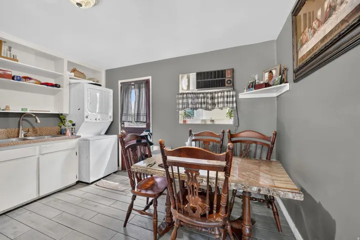 Compact kitchen area featuring wood-finish flooring, white cabinetry, integrated shelving, and a stackable washer and dryer unit