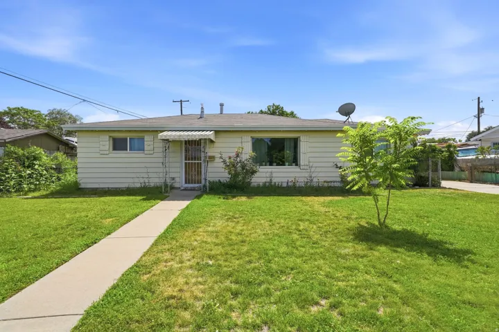 Exterior featuring a light-colored siding, a front entry with an awning, a front yard with grass, a concrete walkway, and a small tree