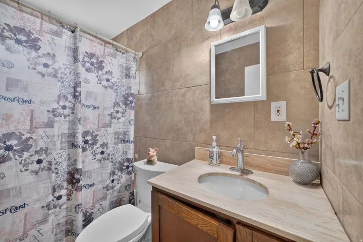 Tile-surround shower with a white toilet, wood-finish vanity with an integrated sink, and an overhead two-light fixture