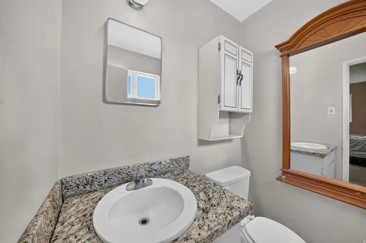 Granite-look countertop, white ceramic sink, wall-mounted cabinet with open shelving, and a large framed mirror