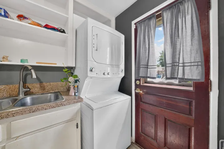 Built-in white shelving, stainless steel sink, speckled countertop, white stacked washer and dryer unit, and a solid wood paneled door
