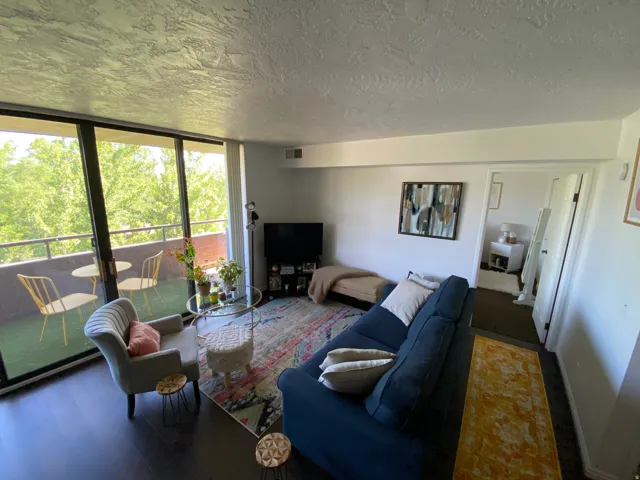 Dark wood-finish flooring throughout, full-wall sliding glass doors leading to a private balcony, and an open doorway reveal an additional room