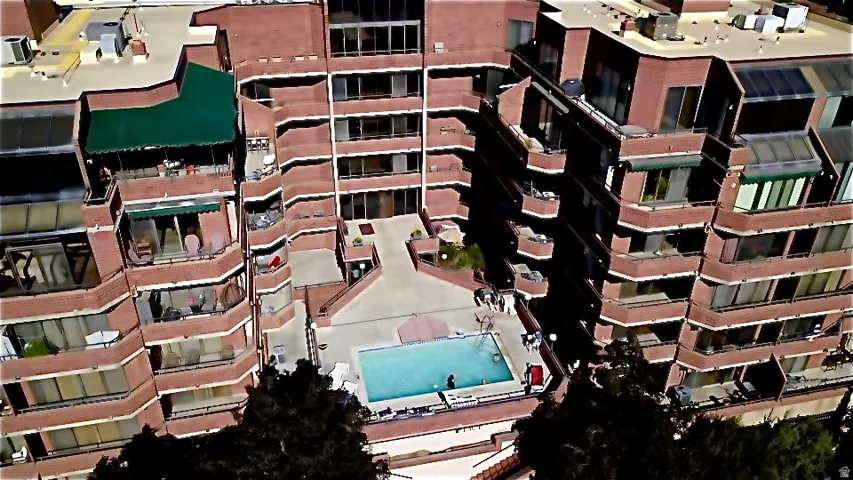 Multi-story building featuring brick-finish exterior, multiple private balconies, and a central swimming pool with surrounding patio