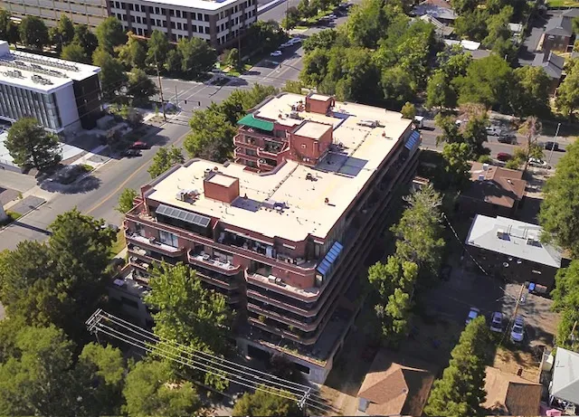 Multi-story building featuring a flat roofline, red brick facade, multiple private balconies, and integrated solar panels
