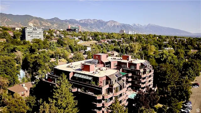 Multi-story residential building featuring extensive balconies, a flat roofline, red brick exterior, and an outdoor pool