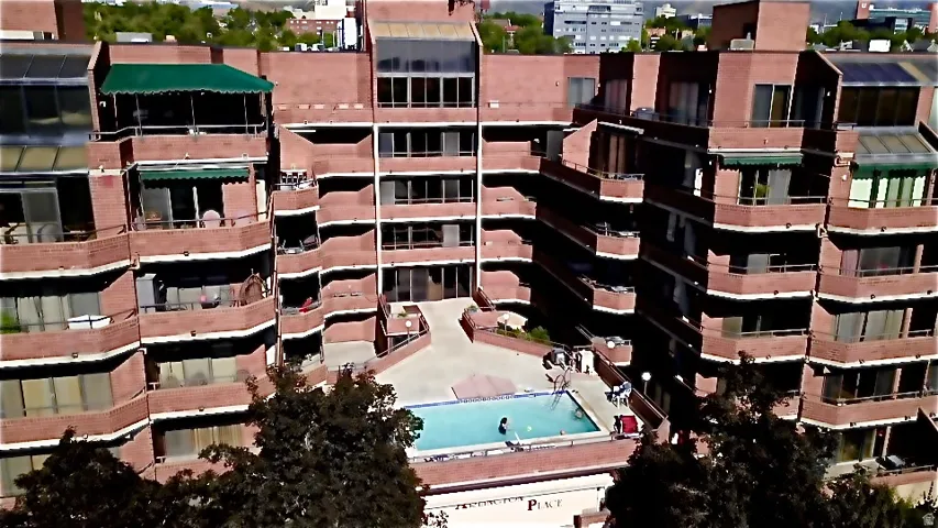 Multi-story brick building with multiple balconies, a central outdoor swimming pool, and a surrounding paved patio area