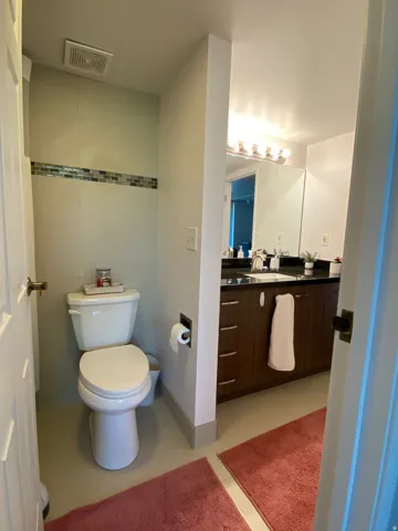 Bathroom featuring a white toilet, tiled walls with a decorative accent band, and a vanity with a dark countertop and wood-finish cabinetry