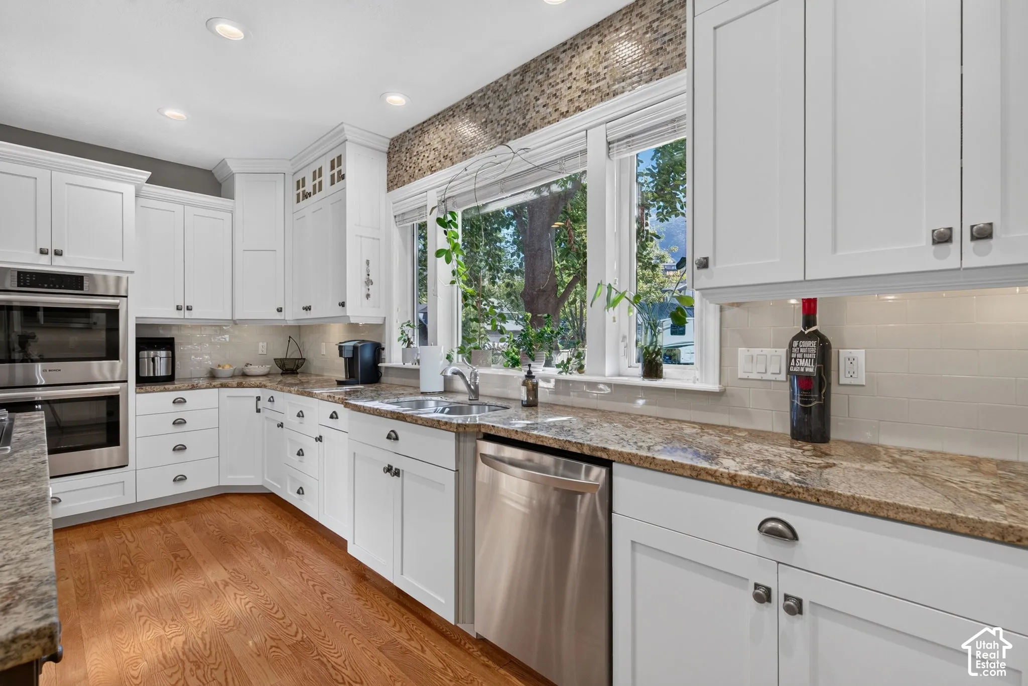 White cabinetry with dark hardware, stone countertops, stainless steel appliances, wood-finish flooring, and recessed lighting