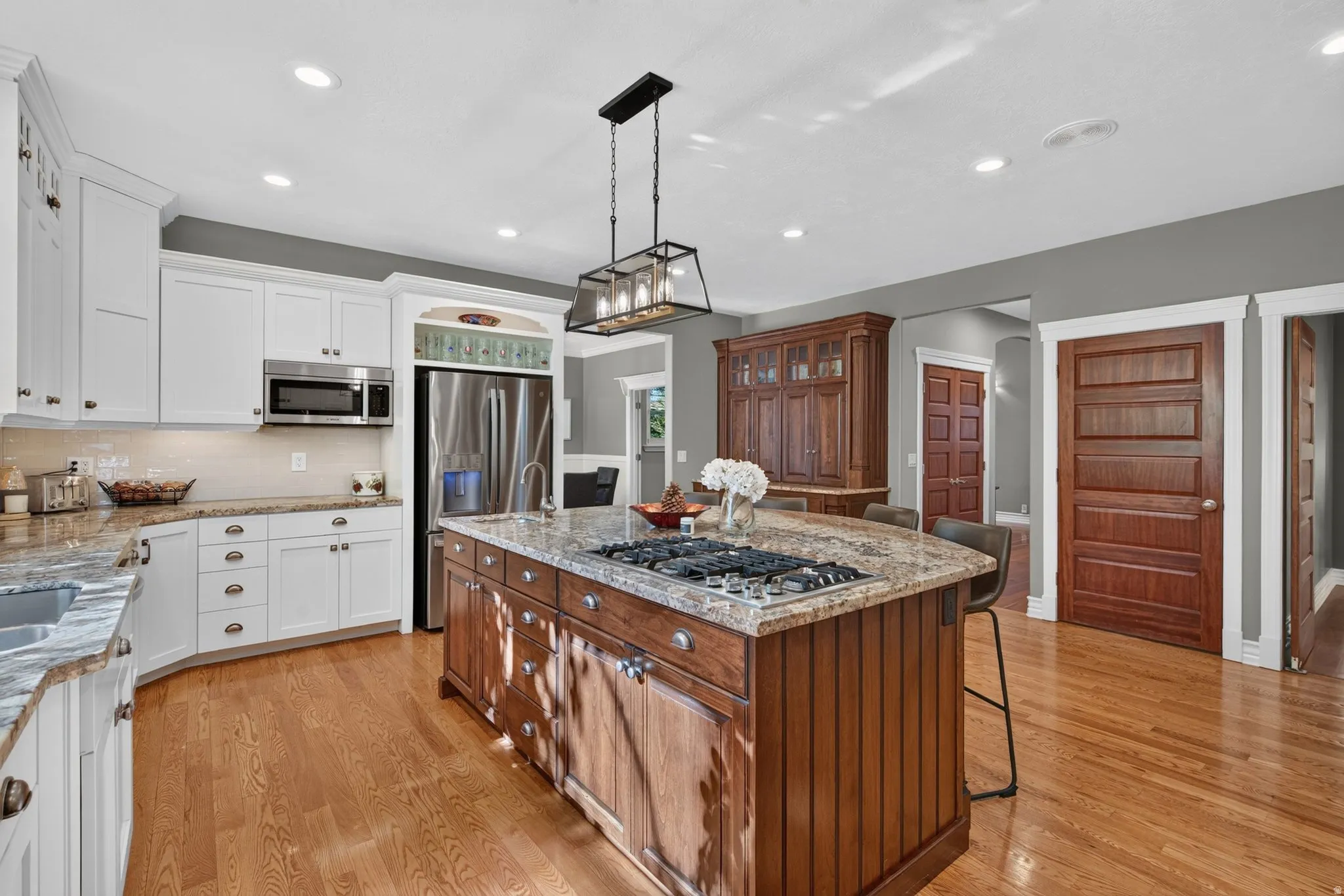 Open-concept kitchen featuring wood-finish flooring, white cabinetry, stainless steel appliances, and a central island with a built-in cooktop and stone-finish countertop