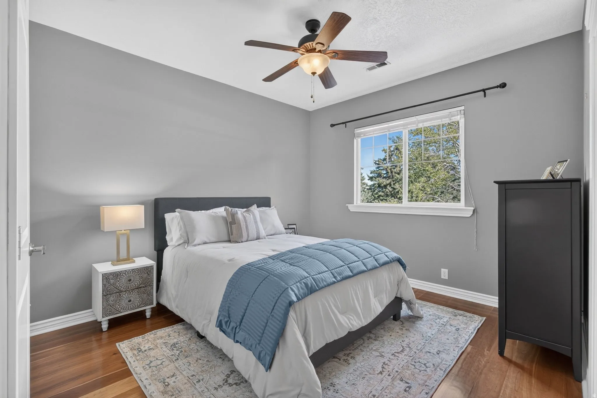 Wood-finish flooring, ceiling fan with integrated lighting, and a window with white trim