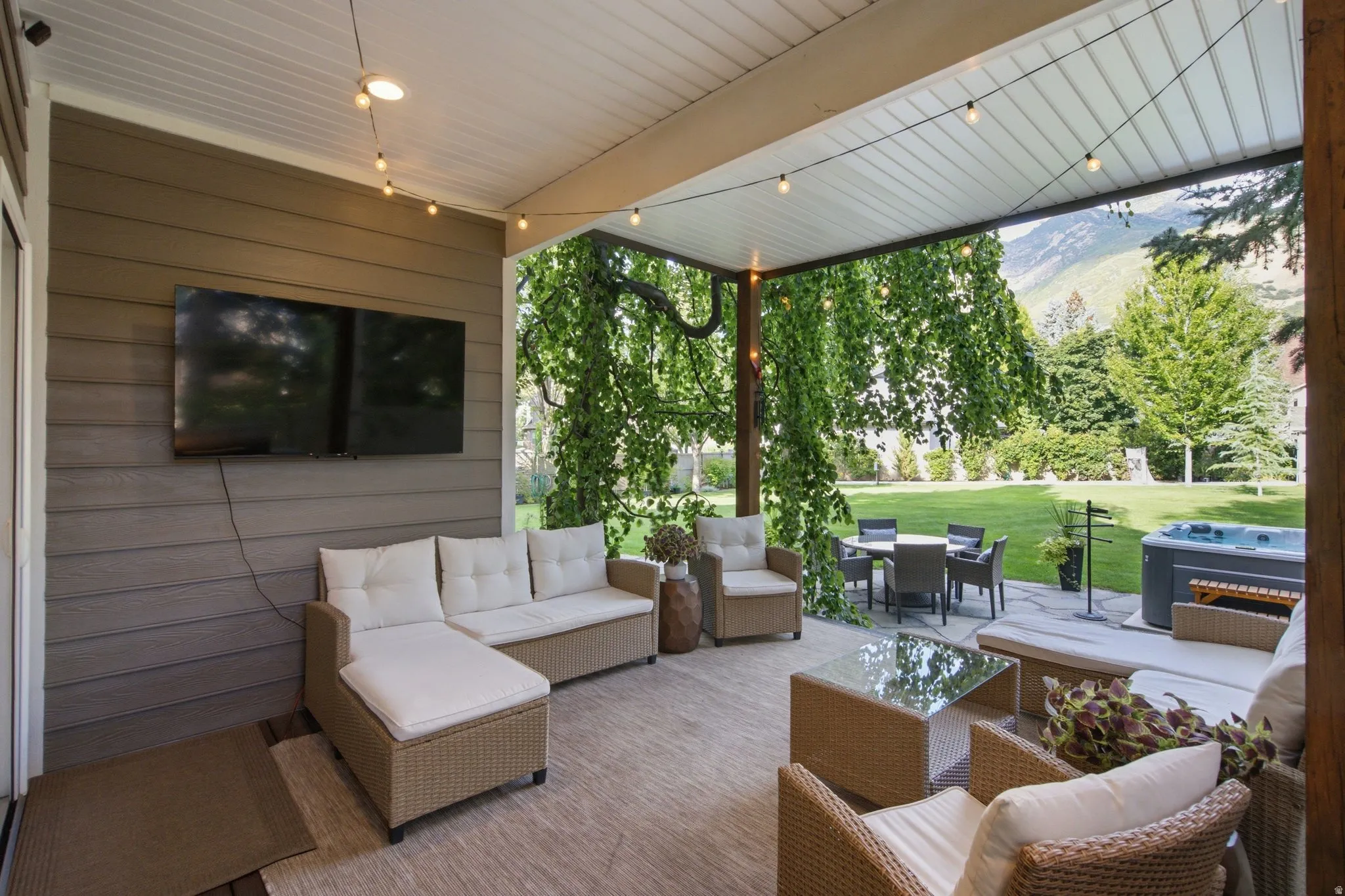 Covered patio featuring an outdoor television, string lighting, and a built-in hot tub