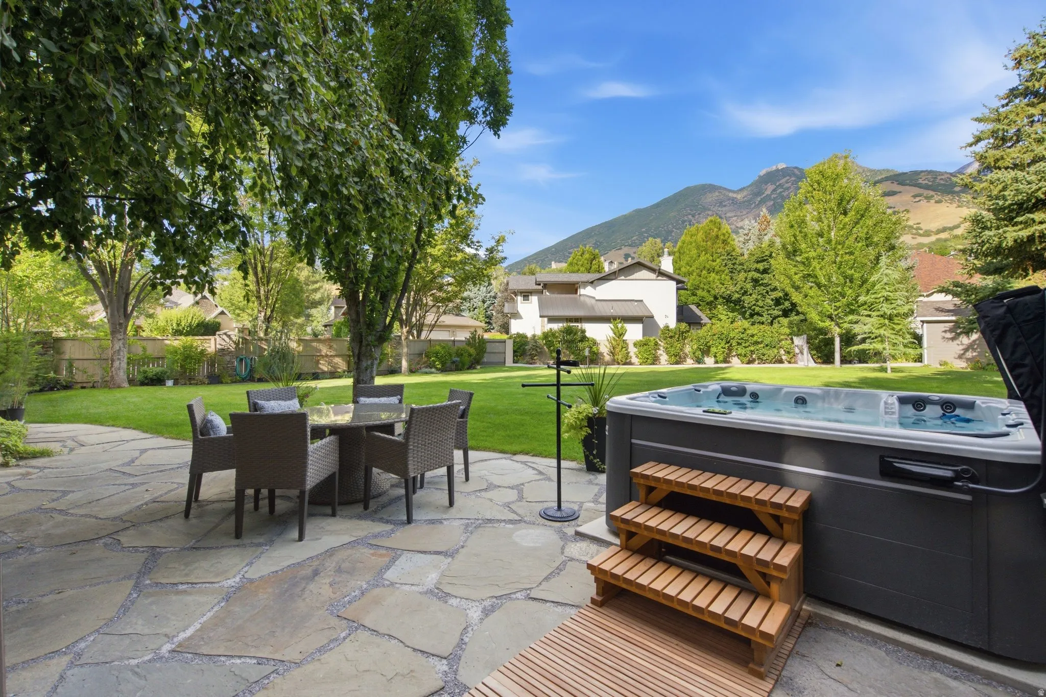 Expansive backyard featuring a natural stone patio, a hot tub with wooden steps, and a lush green lawn