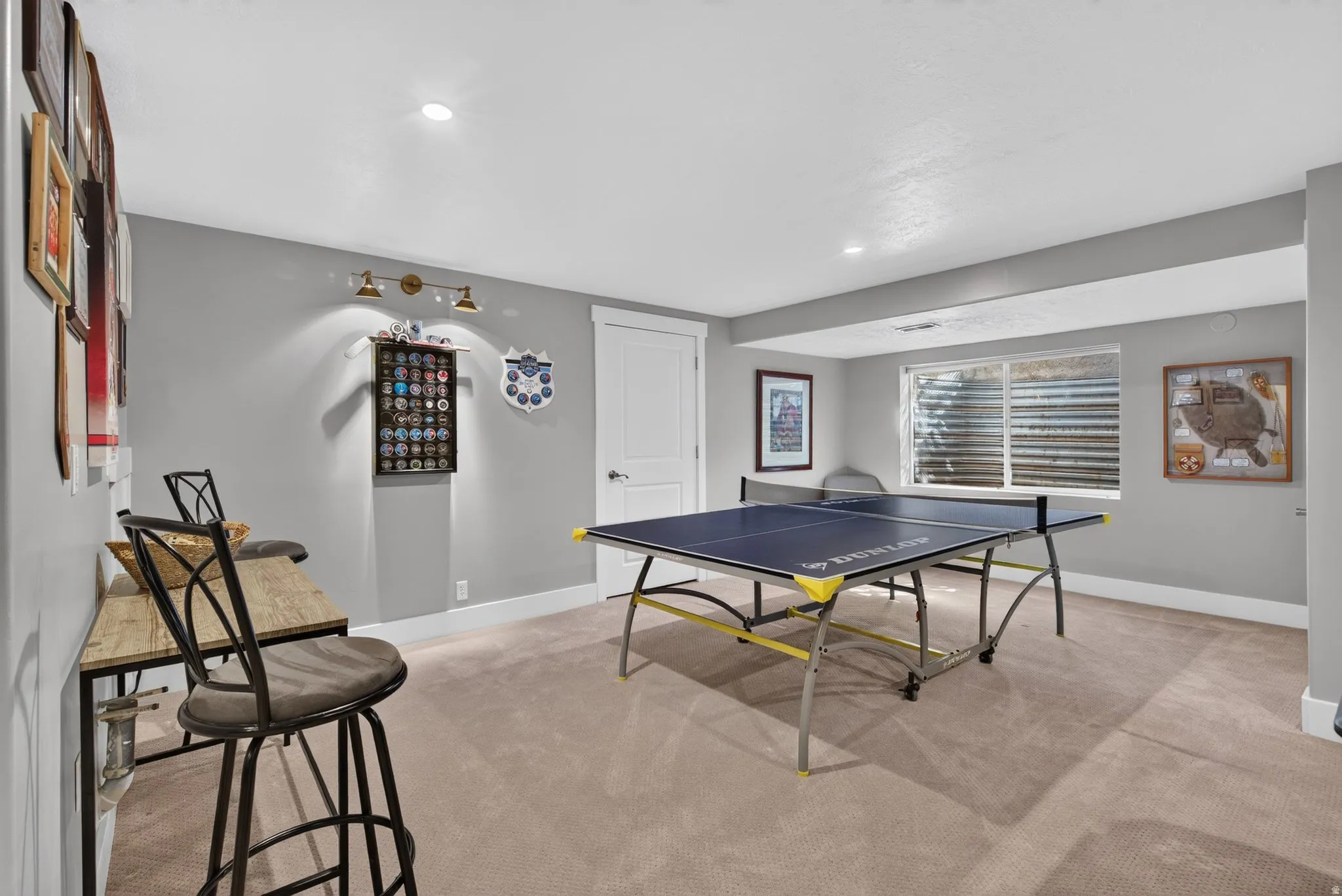 Recessed lighting, wall-mounted fixtures, window with blinds, light gray wall paint, and light-colored carpeting