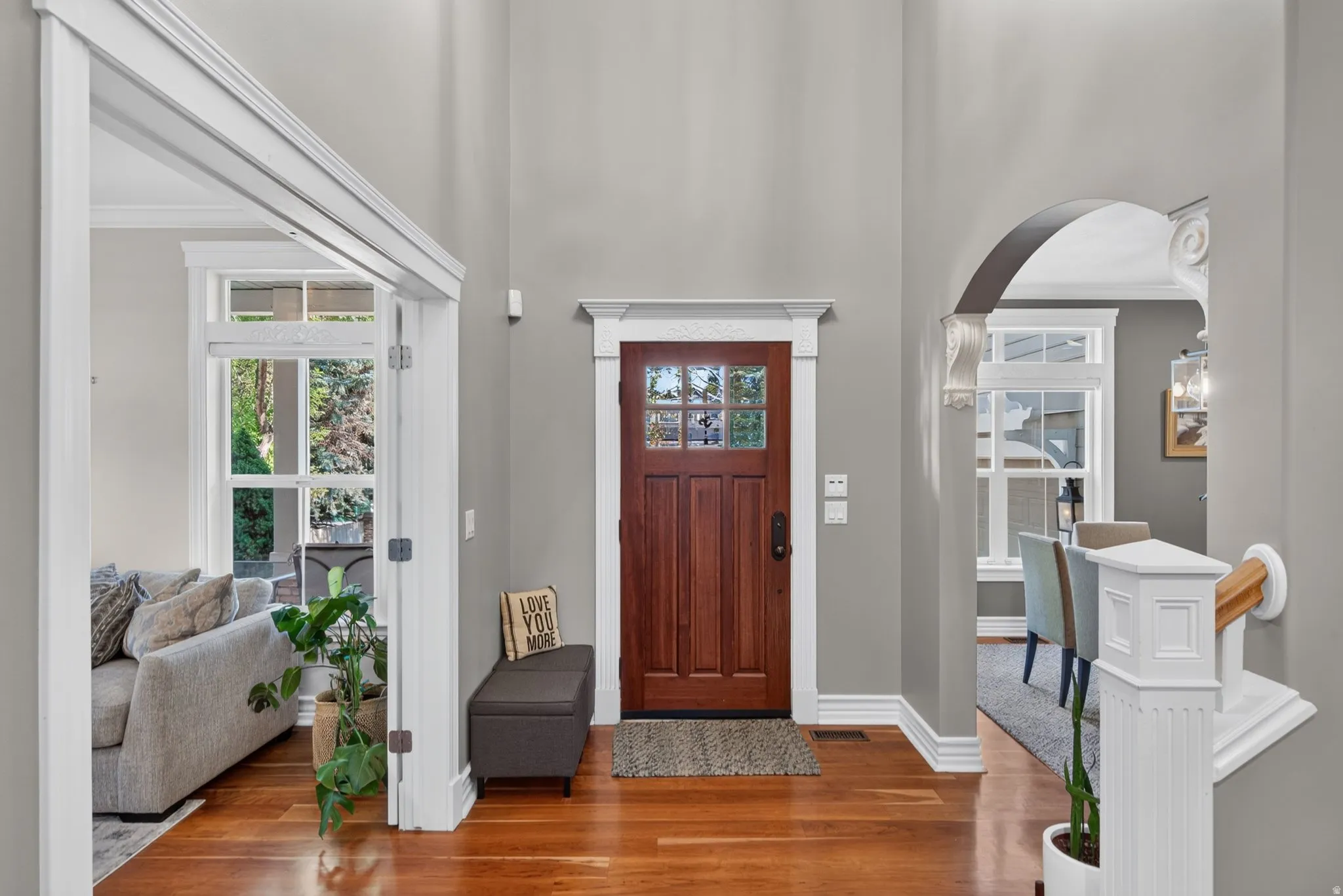Rich wood-finish flooring, a solid wood entry door with glass panes, and decorative trim work