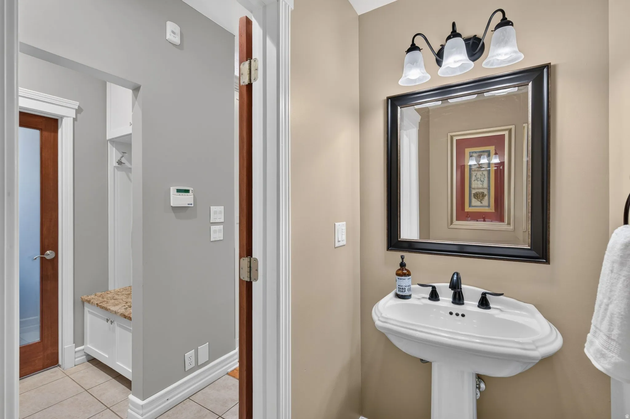 Pedestal sink with black faucet, framed mirror, and three-light vanity fixture