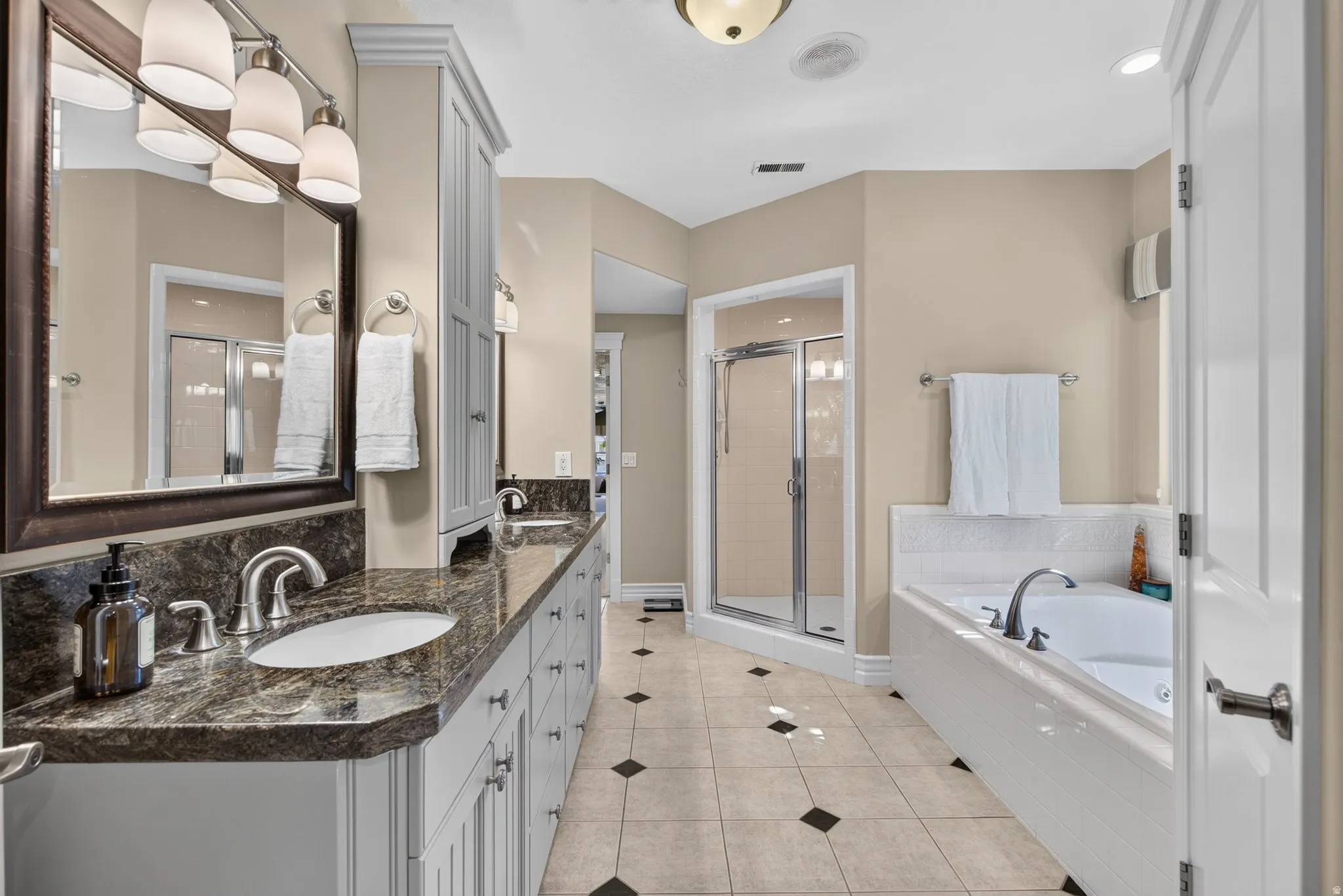 Dual vanity with dark stone countertops, individual sinks, and brushed nickel fixtures