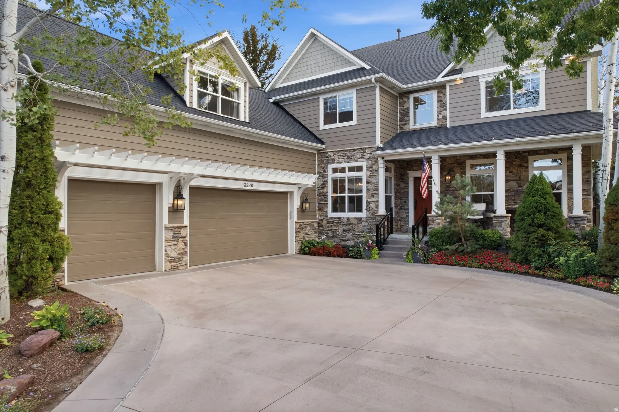 Two-story residence featuring a stone and siding exterior, multi-pane windows, covered entry with pillars, and an attached two-car garage with pergola accents