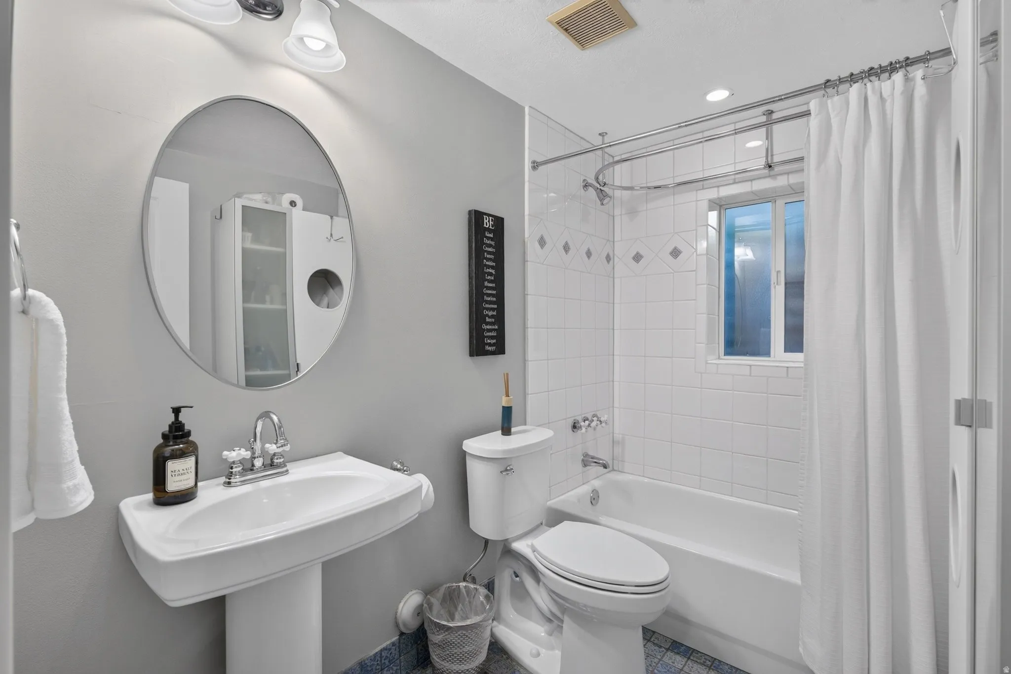 Pedestal sink with a chrome faucet, oval mirror, white subway tile shower surround with accent tiles, and a built-in window