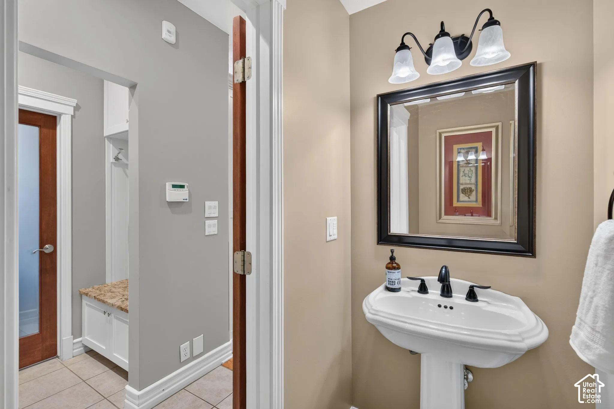 Pedestal sink with black faucet, framed mirror, and three-light vanity fixture