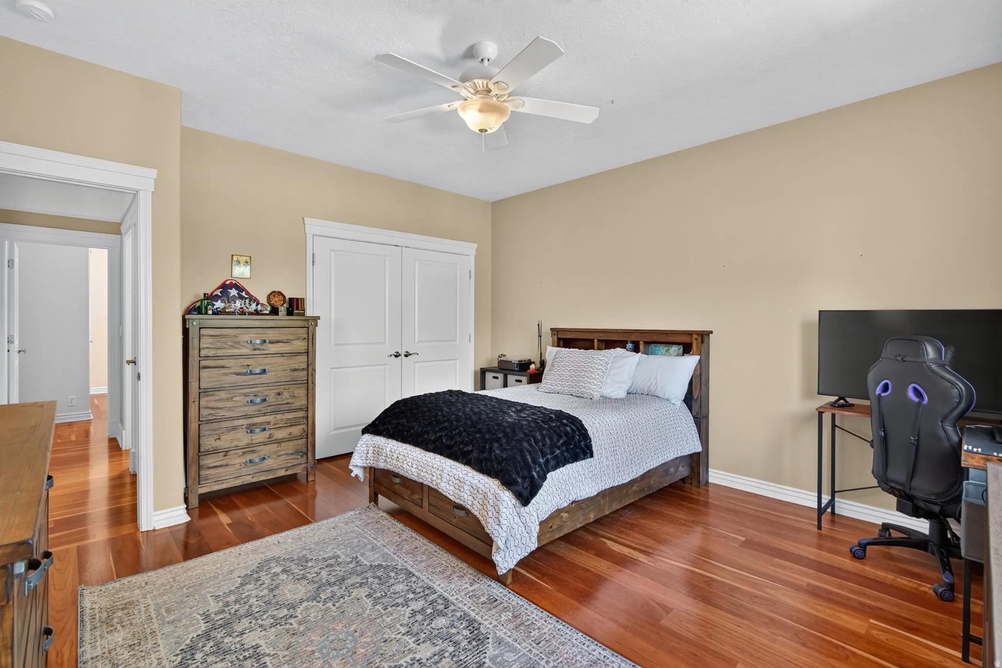 Warm-toned wood-finish flooring, a ceiling fan with integrated lighting, and white bi-fold closet doors