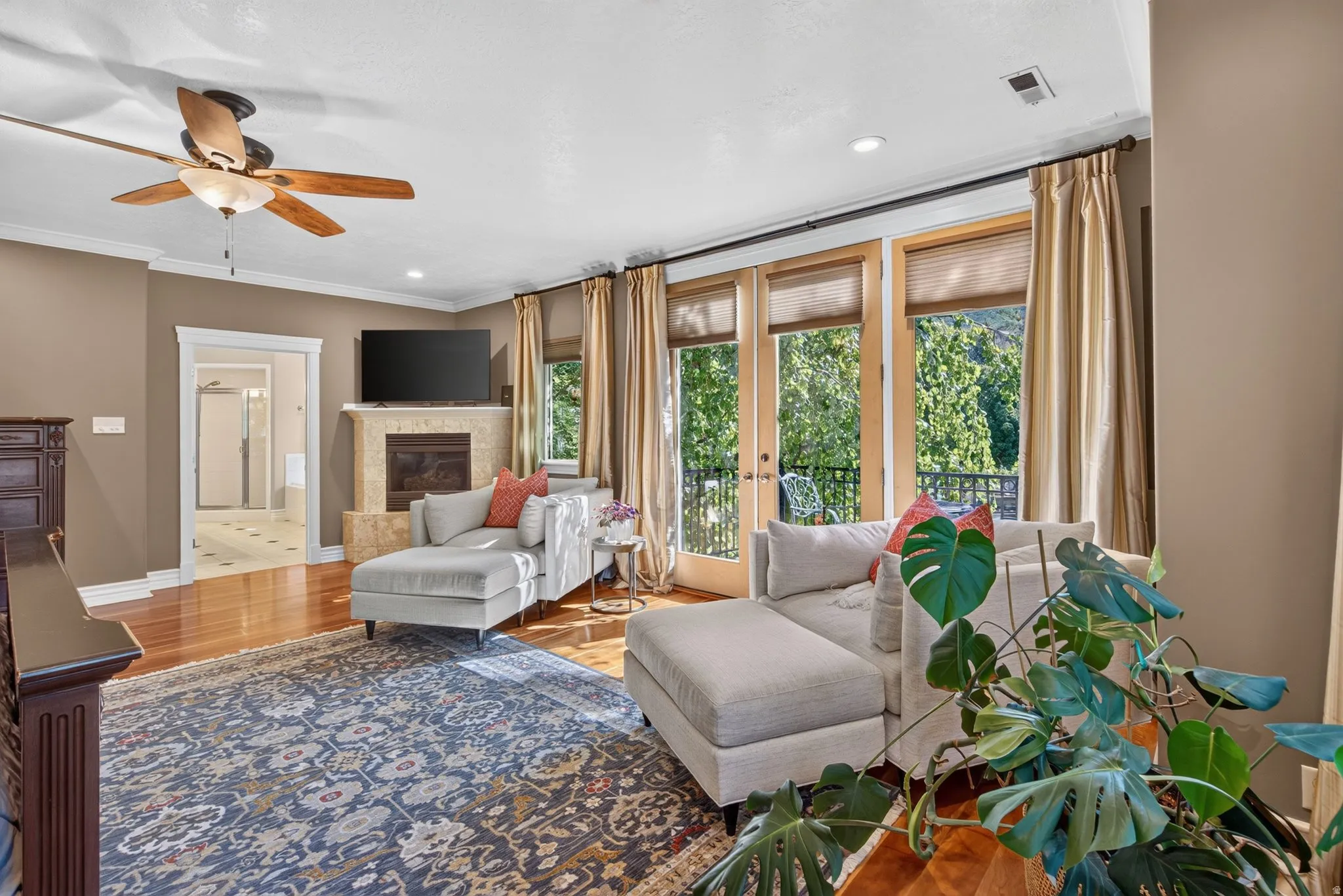 Hardwood flooring throughout, a ceiling fan with integrated lighting, and a stone-clad fireplace