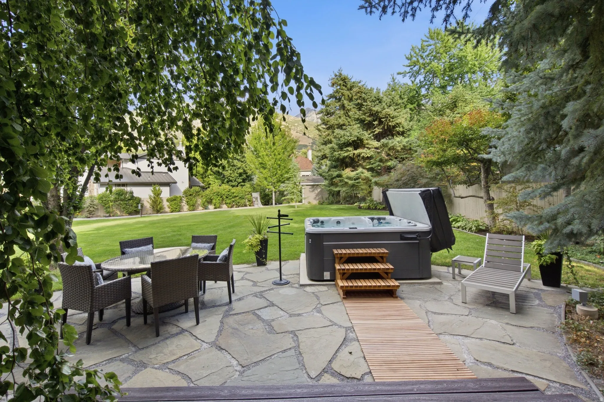 Expansive flagstone patio with a built-in hot tub, complemented by a large manicured lawn and mature trees