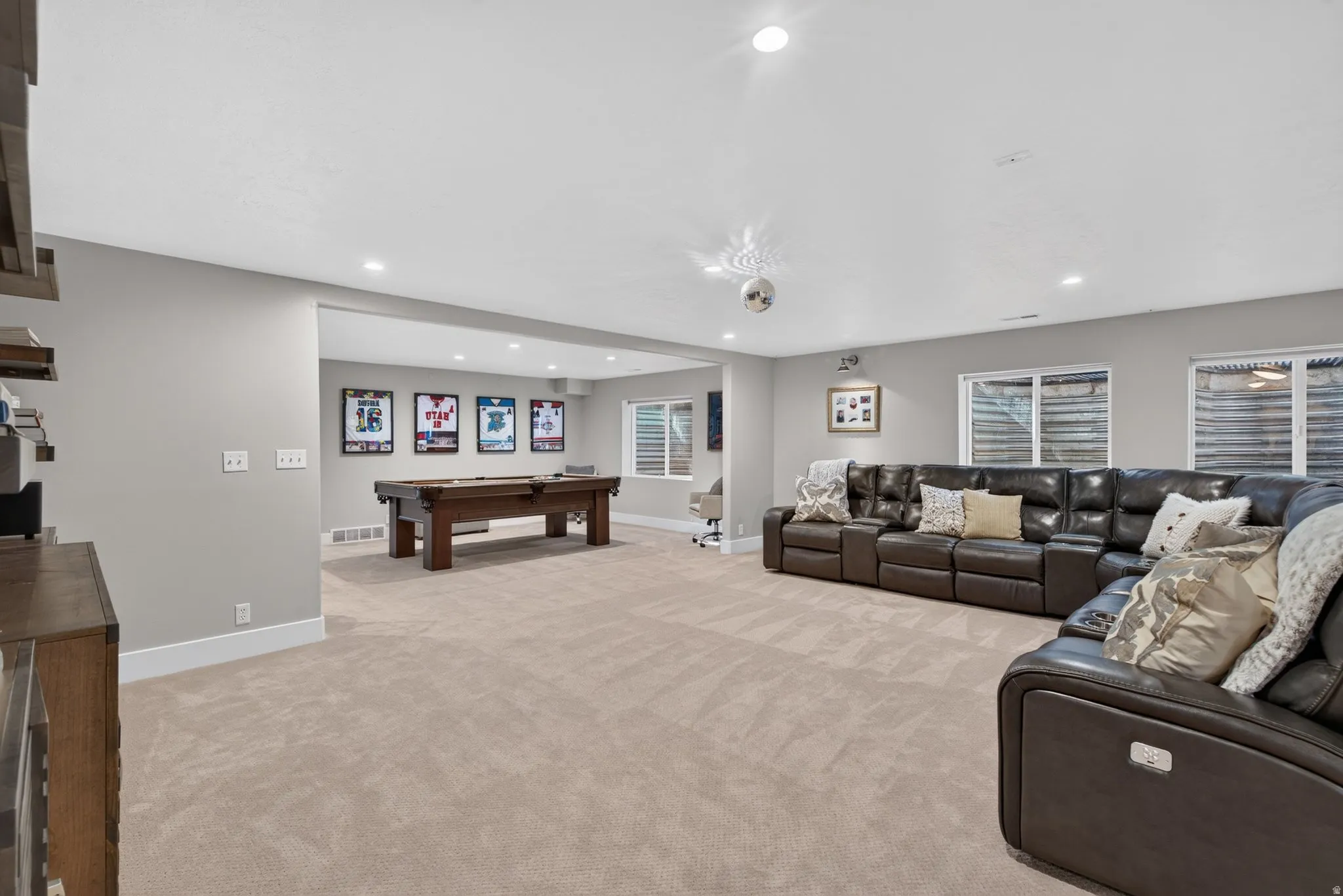 Recessed lighting illuminates the expansive carpeted flooring, complemented by multiple wall-mounted windows