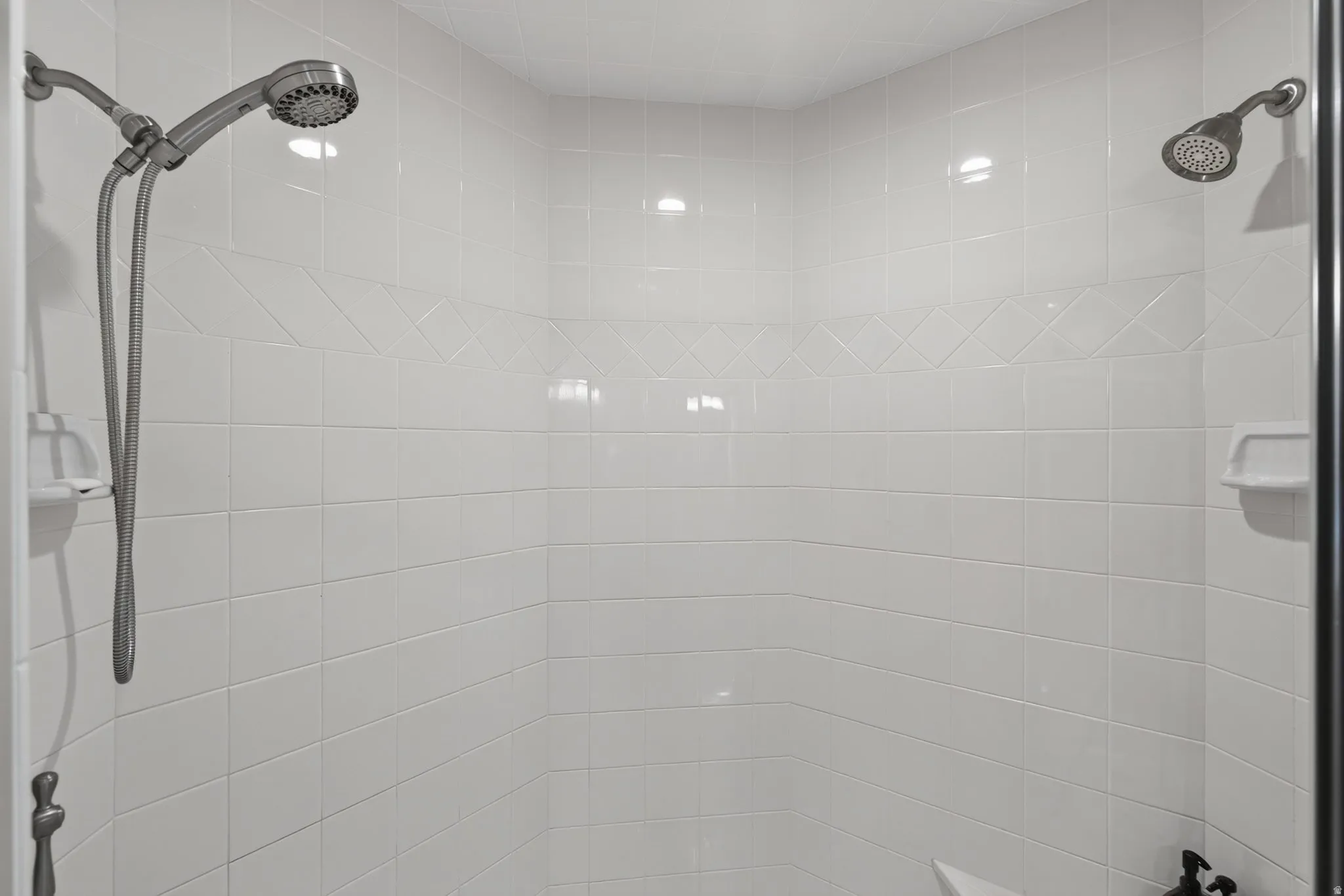 Shower enclosure featuring white ceramic tile walls, decorative accent tile band, fixed shower head, and an additional handheld shower fixture