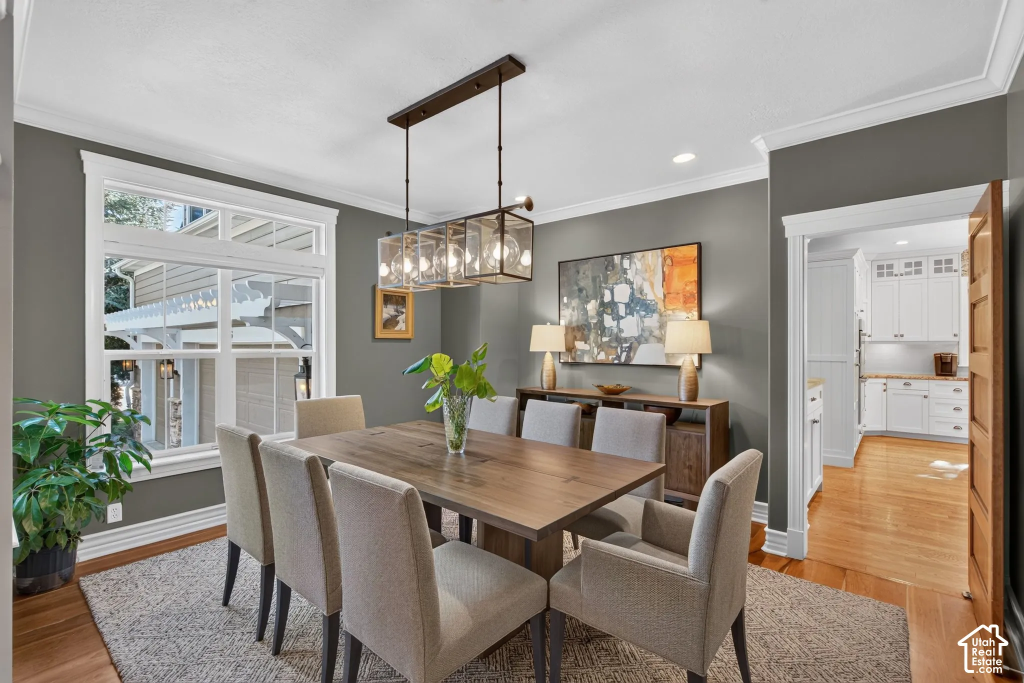 Dining area featuring wood-finish flooring, a large window with transom, crown molding, and a multi-light linear chandelier