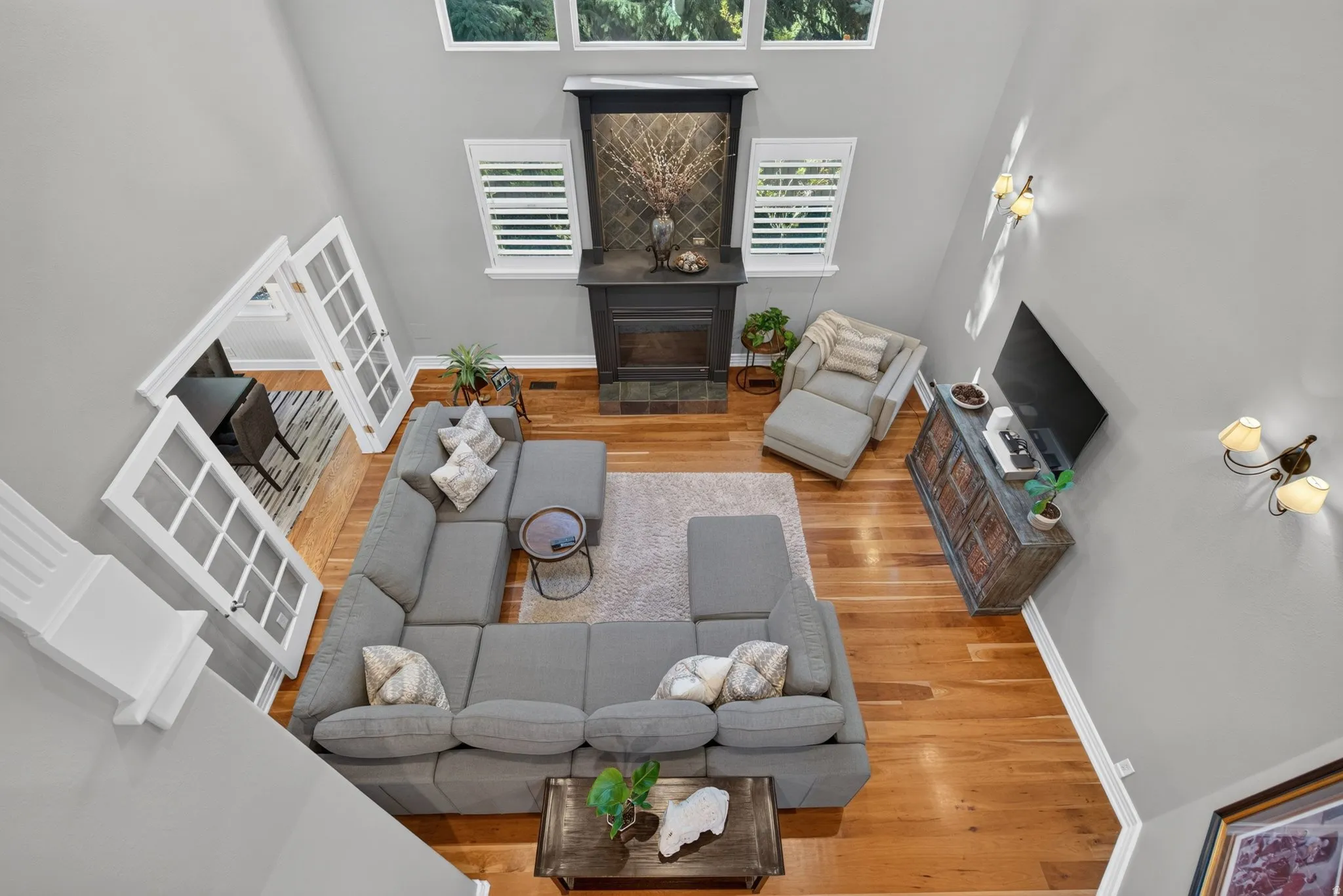 High vaulted ceiling with upper windows, wood-finish flooring, a fireplace featuring a dark mantel and tile surround, and French doors