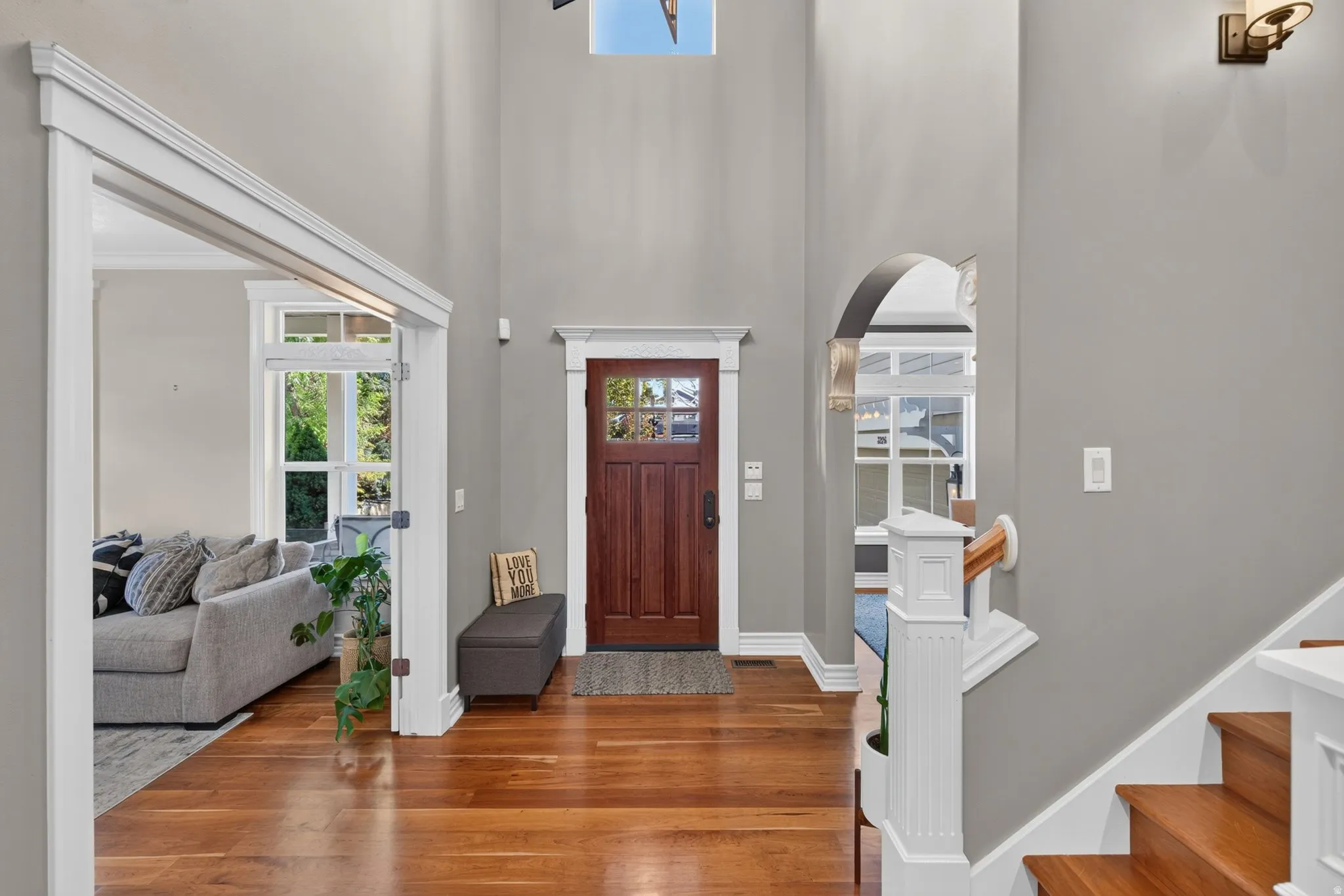 High ceilings, wood-finish flooring, solid wood entry door with glass panels, white trim, and a staircase with wood treads and white risers